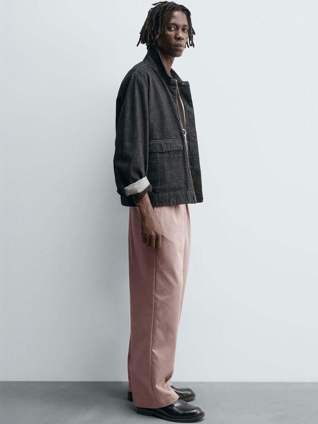 Men Pleated Trousers in relaxed fit pink color, styled with a black jacket, perfect for a trendy look.